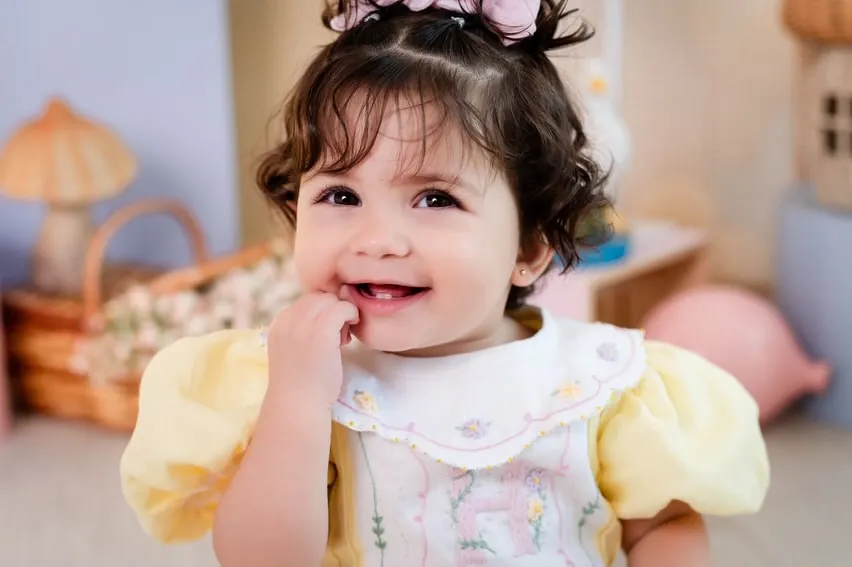 Bebê sorrindo com vestido amarelo e gola bordada
